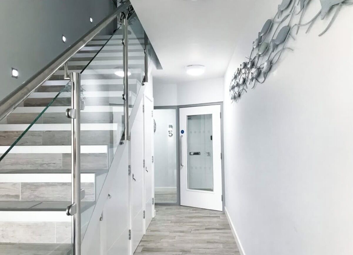 Un intérieur moderne avec un escalier en verre, un couloir avec une porte et un luminaire fixé au mur.