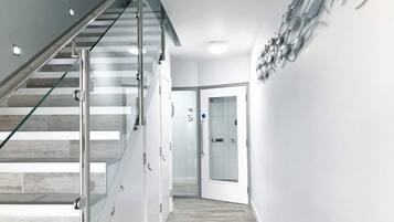 Un intérieur moderne avec un escalier en verre, un couloir avec une porte et un luminaire fixé au mur.