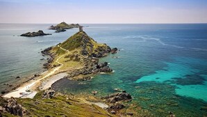 Un paisaje costero con una colina destacada, un faro y aguas azules cristalinas.