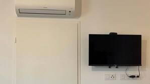 Una puerta blanca con manija plateada, un aire acondicionado instalado y un televisor de pantalla plana en la pared.