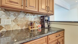 A kitchen with wooden cabinets, a marble backsplash, a coffee maker, and a spice rack.