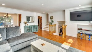 A modern living room with a grey sofa, white coffee table, wooden flooring, a staircase, and a large flat-screen TV mounted on the wall.
