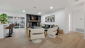 A modern living room with a fireplace, a dining area with bar stools, and a sofa set. - Indoor Pool & Hot Tub Near AT&T Stadium (Irving)