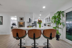 Cozinha moderna com ilha central, três banquetas de madeira e uma grande planta em vaso.
