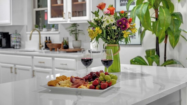 A marble countertop with a charcuterie board, two glasses of red wine, and a vase of flowers. - Indoor Pool & Hot Tub Near AT&T Stadium (Irving)