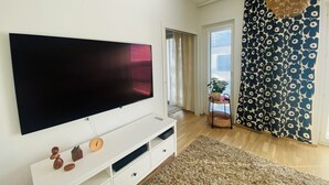 A living room with a large flat-screen TV, a white entertainment unit, a patterned curtain, and a view of the outdoors. - Nordic Home Bliss With Marimekko Moments (Helsinki)