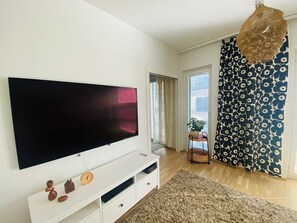 Olohuone, jossa on suuri litteänäyttöinen televisio, valkoinen mediakeskus, kuviollinen verho ja näkymä ulos.