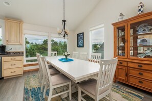 Una cocina moderna con un amplio comedor, armarios blancos y vistas a la vegetación.