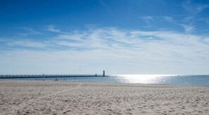 Una spiaggia con un molo che si protende nell'acqua, un faro all'estremità del molo e un cielo sereno.