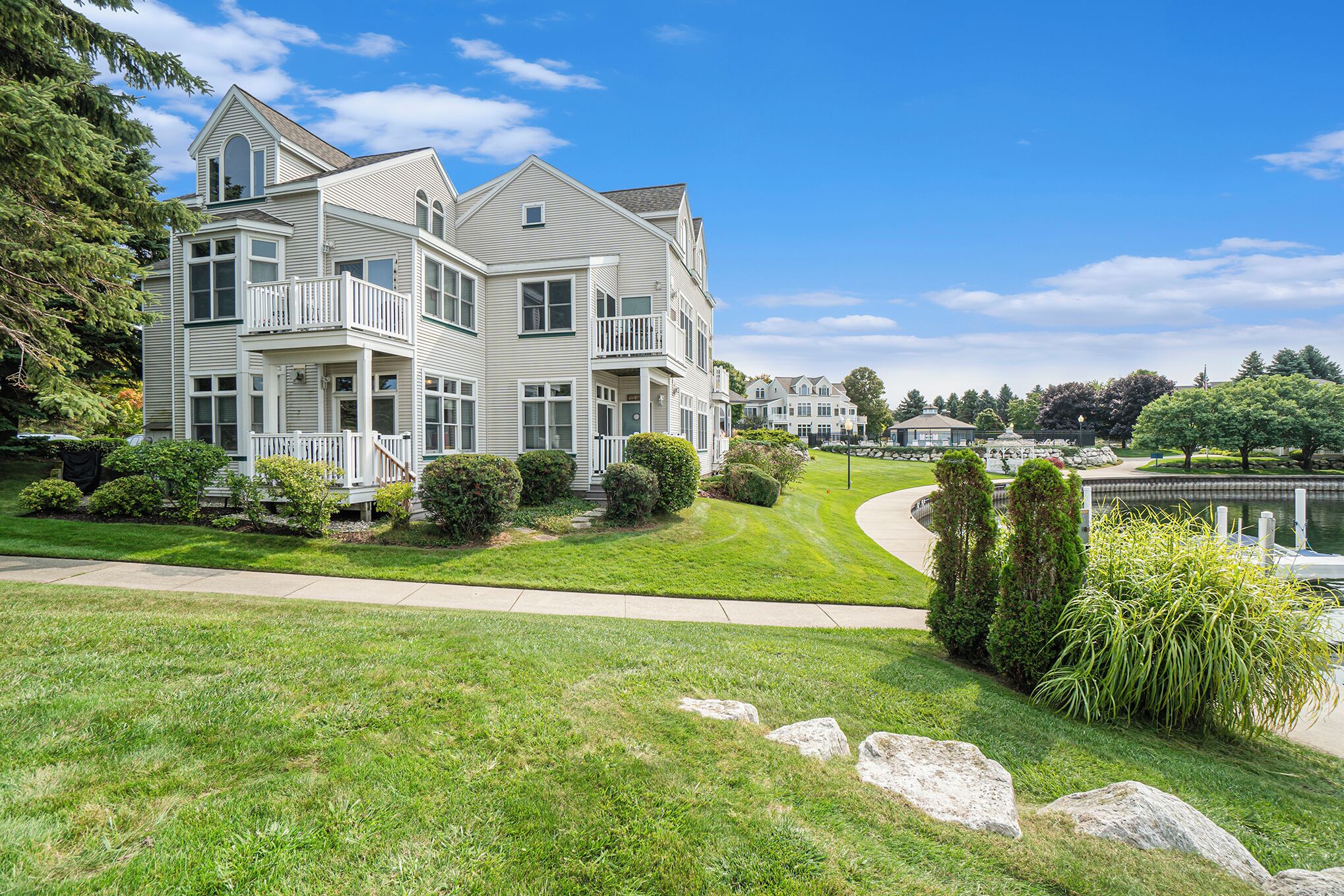 A large, two-story house with a balcony, surrounded by well-maintained lawns and a small pond.