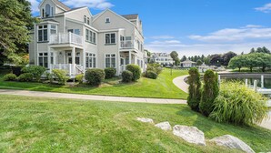 A large, two-story house with a balcony, surrounded by well-maintained lawns and a small pond. - Marina Studio- King Bed, No Steps (Manistee)