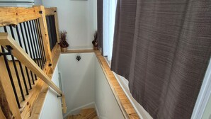 Un escalier en bois avec une rampe, une petite fenêtre et un tableau accroché au mur.