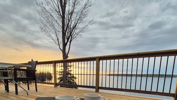 Une terrasse avec un plateau rempli de tasses blanches, une chaise en osier et une vue sur l’eau.