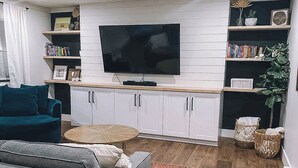 Un soggiorno moderno con televisione a schermo piatto, mobili bianchi, un divano grigio e un tappeto colorato.