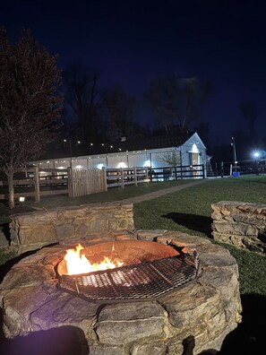 Un foyer en pierre avec une grille en métal, entouré d’un muret en pierre, situé dans un espace extérieur bien éclairé la nuit.