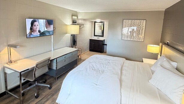 A hotel room with a bed, desk, chair, TV, and a wall with a framed picture. - Deluxe Inn (Mauldin)