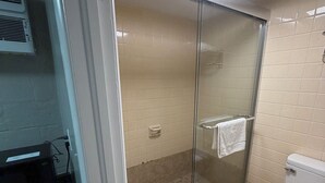 A bathroom with a glass shower enclosure, a toilet, and a sink area. - Deluxe Inn (Mauldin)