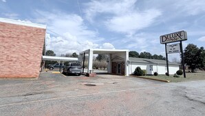 A hotel entrance with a sign for 'Deluxe Inn' and a parking lot with a few cars. - Deluxe Inn (Mauldin)