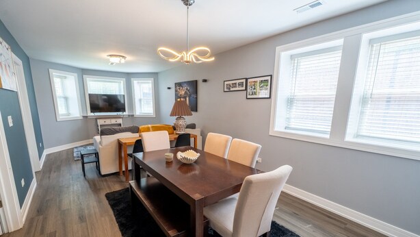 A dining area with a wooden table, white chairs, a black rug, and a ceiling light fixture. - 2 Bedroom apartment free parking near transit (Chicago)