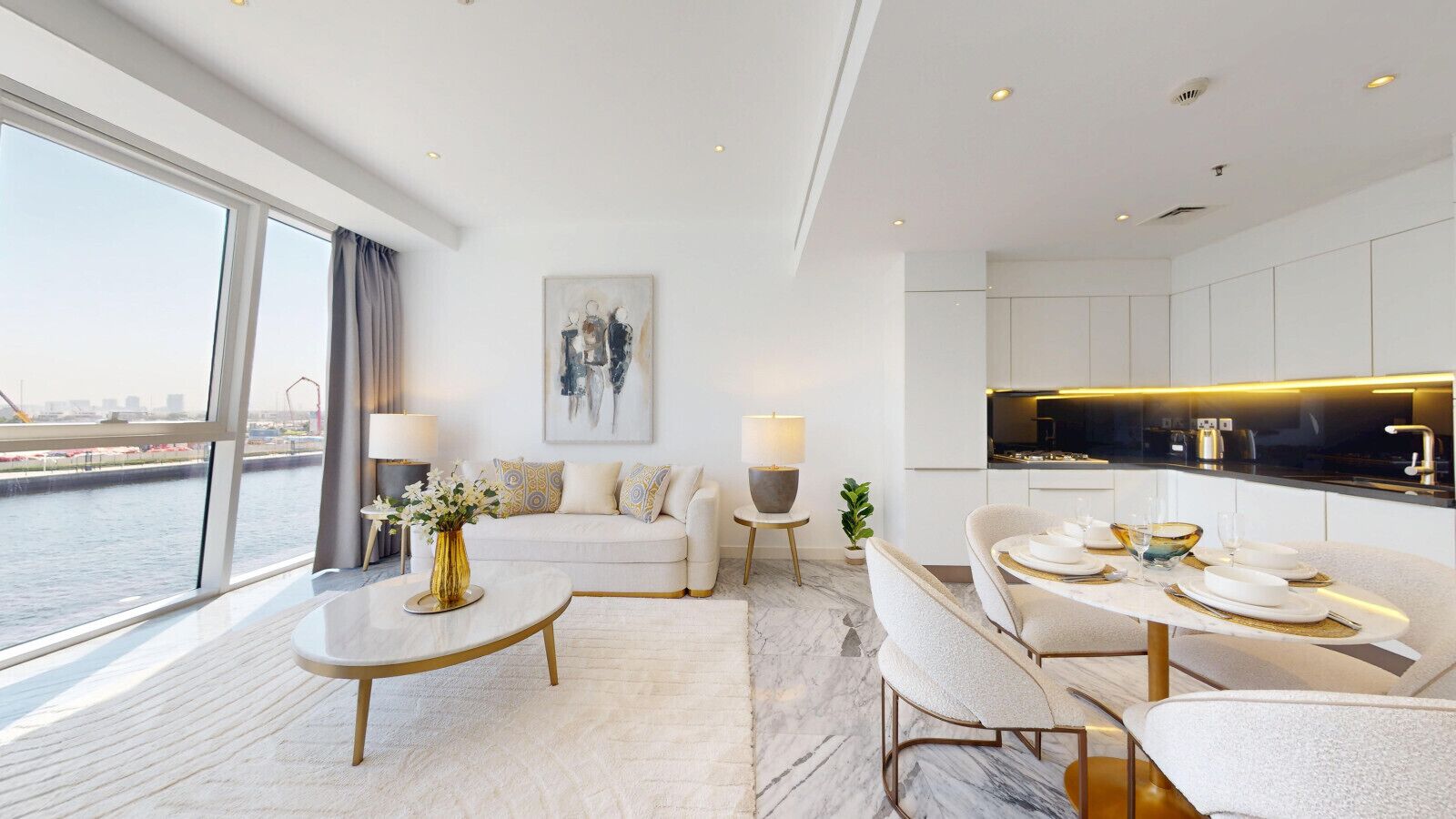 En moderne stue med sofa, sofabord og spiseplads. Der er et stort vindue med udsigt over vandet.