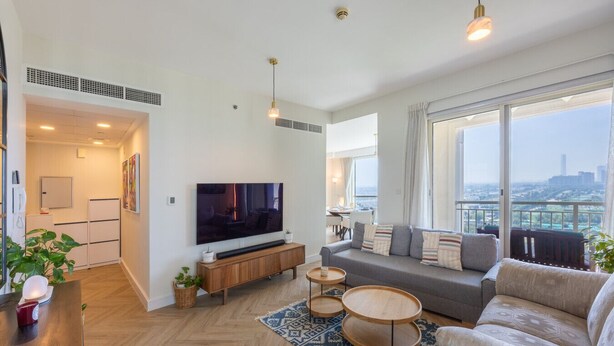 A modern living room with a large TV, a sofa, a coffee table, and a view of the city. - Vibrant 2 Bed l The Greens l Family Retreat (The Greens)