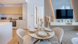 Una cocina moderna con armarios de madera, un comedor con una mesa redonda para cuatro personas, y un televisor de pantalla plana grande montado en la pared.
