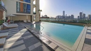 Una piscina en la azotea con vistas al horizonte de la ciudad, sillas de descanso y una barandilla de cristal.