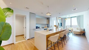 Una cocina moderna con armarios blancos, una isla central con taburetes y un comedor con sofá y sillas.