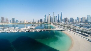 A coastal cityscape with a marina, high-rise buildings, and a sandy beach. - Modern 1 Bed l Private Beach l Pool, Gym Access (Emaar Beachfront)