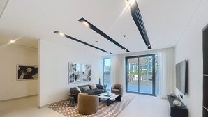 A modern living room with a sofa, armchairs, a coffee table, and a TV. - Modern 1 Bed l Private Beach l Pool, Gym Access (Emaar Beachfront)