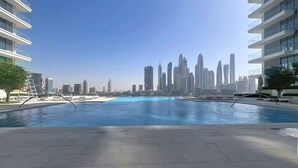 A swimming pool with a city skyline in the background. - Modern 1 Bed l Private Beach l Pool, Gym Access (Emaar Beachfront)