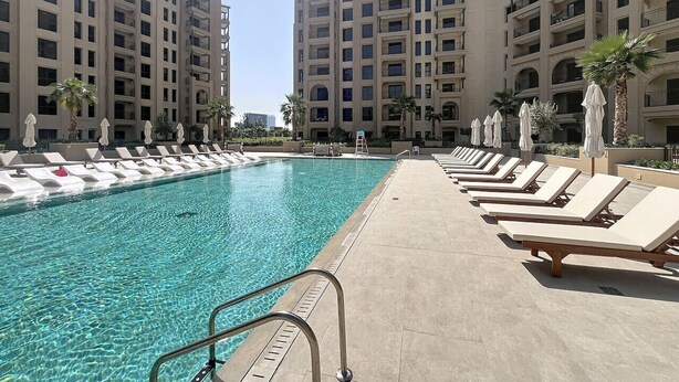 A swimming pool with lounge chairs and umbrellas, surrounded by high-rise buildings. - Luxury Living 1 Bed l Pool View l Burj Al Arab (Madinat Jumeirah Living)