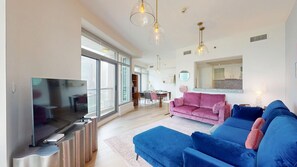 A modern living room with a large flat-screen TV, a pink sofa, and a blue sofa. - Vibrant 2 Bed l City Skyline Views l Marina Walk (Dubai Marina)