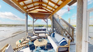 A covered outdoor seating area with a wooden deck, a swing, and a view of a river and beach.