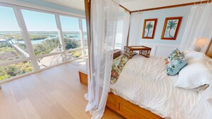 A bedroom with a large window, a bed with a canopy, and two framed pictures on the wall.