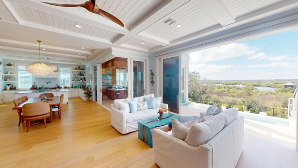 A spacious living area with a large window overlooking a scenic landscape, a dining area with wooden furniture, and a kitchen with white cabinetry.