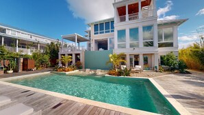A modern two-story house with a large swimming pool, outdoor furniture, and lush landscaping.