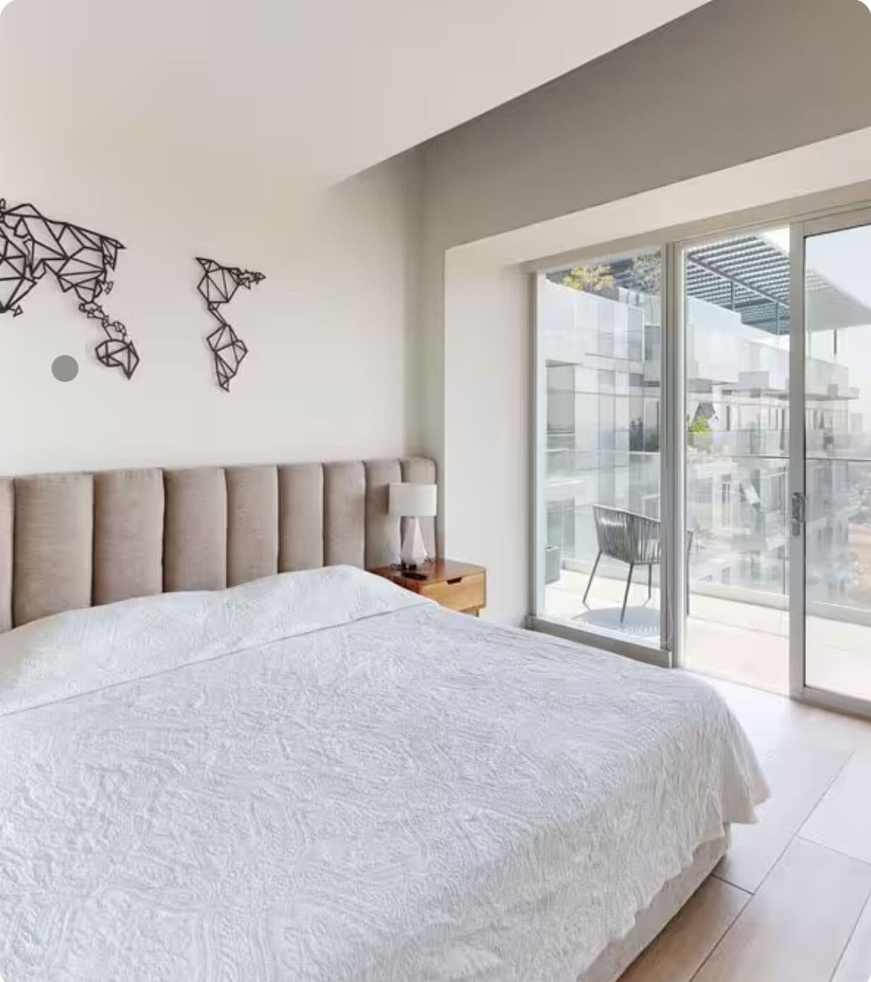 A modern bedroom with a large bed, a nightstand, and a view of the city through large windows.