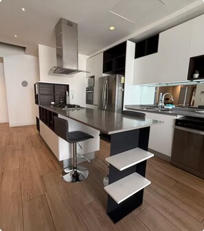 A modern kitchen with a central island, stainless steel appliances, and a bar stool seating area. - Amazing 3 bedroom Apartment Loby 33 (Zapopan)