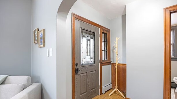 Un pasillo con una puerta de madera, un perchero y un sofá de color claro.