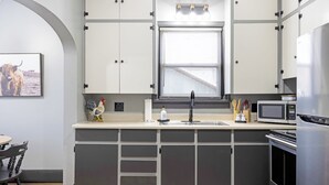 Una cocina moderna con microondas integrado, refrigerador de acero inoxidable y ventana con persianas.