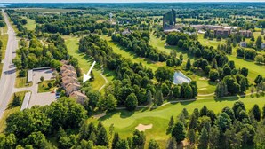 Et luftfoto af en golfbane med et moderne bykompleks, omgivet af frodigt grønt og en klar himmel.