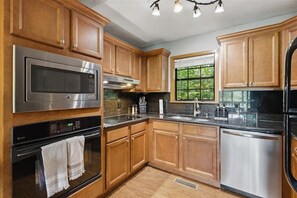 A kitchen with wooden cabinets, stainless steel appliances, a window, and a black countertop. - Above It All | Hot Tub + Smoky Mtn Views - Holiday Home (Pigeon Forge)