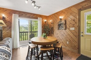 A wooden-paneled room with a round table and four chairs, a bed, a window with curtains, and a door. - Unobstructed Smoky Mountain Views, Hot Tub, Pigeon Forge (Pigeon Forge)