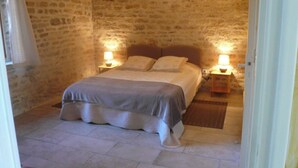 A stone-walled bedroom with a bed, two bedside lamps, and a wooden nightstand.