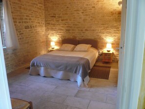 Une chambre aux murs de pierre, avec un lit, deux lampes de chevet et une table de nuit en bois.