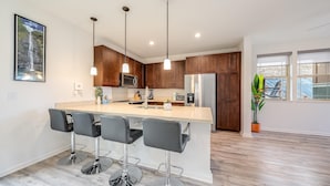 A modern kitchen with a central island, bar stools, wooden cabinets, and pendant lighting.