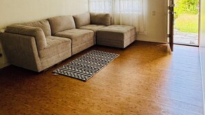 Un salon avec un canapé d’angle beige, un ventilateur de plafond et un tapis à motifs.