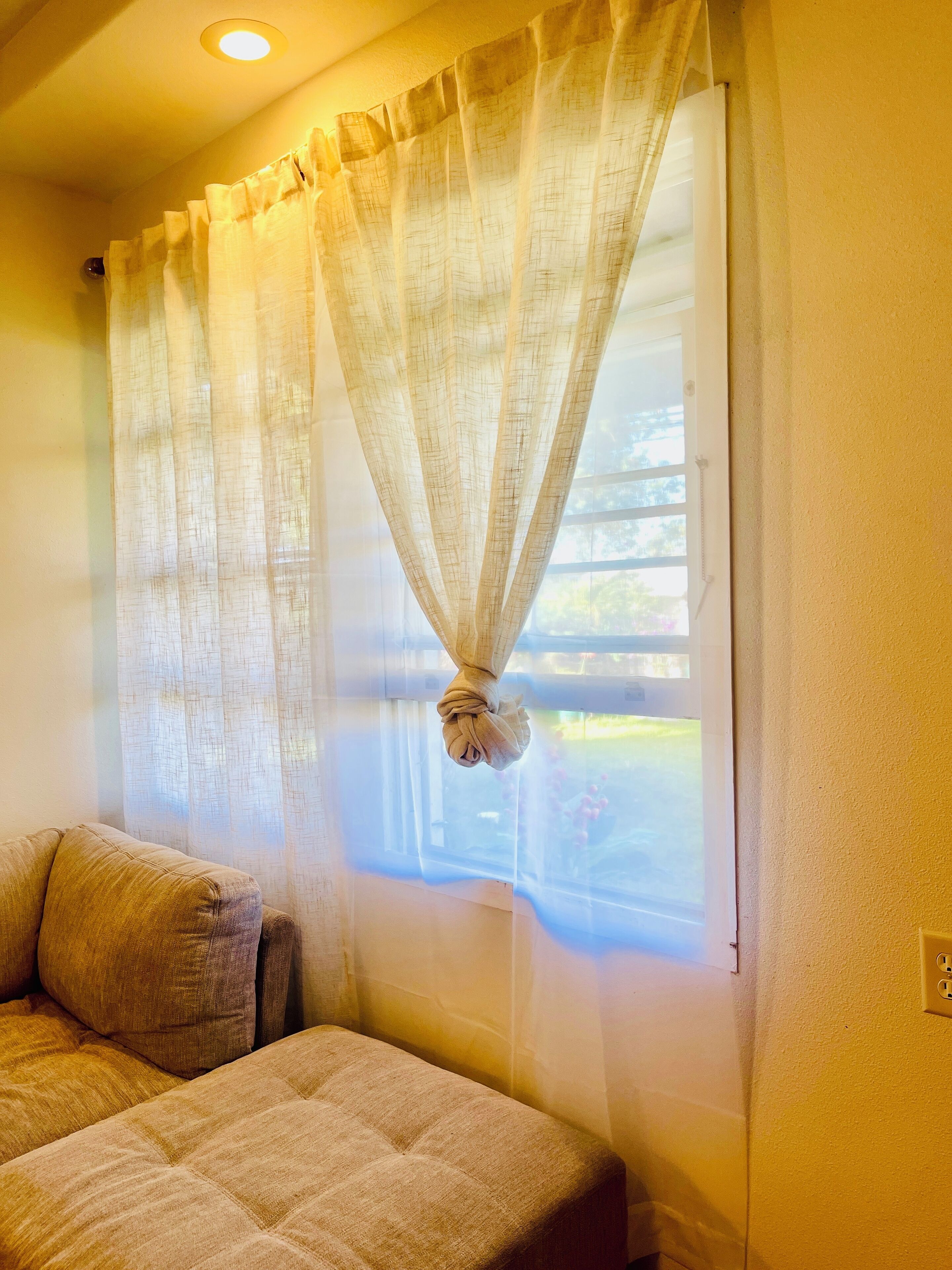Un dormitorio con cama, ventana con cortinas traslúcidas y vistas al exterior.