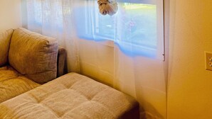Une chambre à coucher avec un lit, une fenêtre ornée de rideaux légers et une vue dégagée sur l’extérieur.